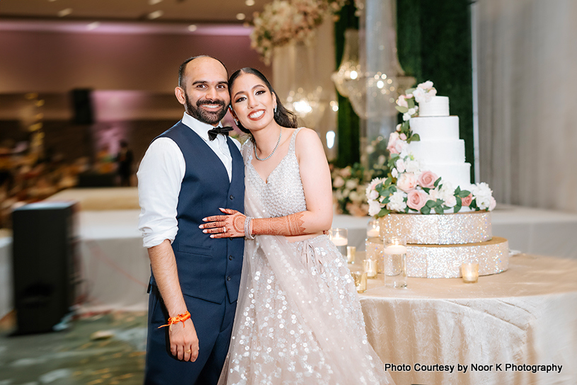 Indian wedding couple posing for photoshoot near wedding cake
