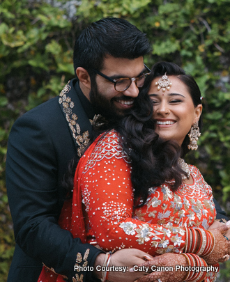The bride and groom sharing a joyful moment outdoors, dressed in coordinated ivory and gold Indian wedding outfits.