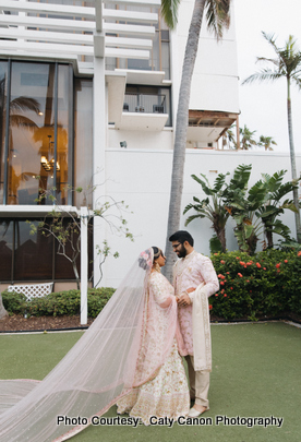 A beautiful outdoor portrait of a couple dressed in intricate Indian wedding garments, smiling at each other.