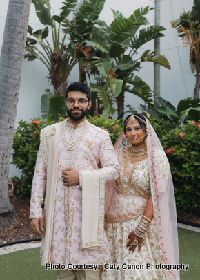 he bride and groom sharing a joyful moment outdoors, dressed in coordinated ivory and gold Indian wedding outfits.