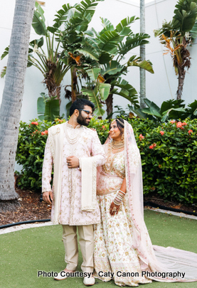 Ami and Vinny walking together in pastel traditional wedding attire with tropical plants in the background