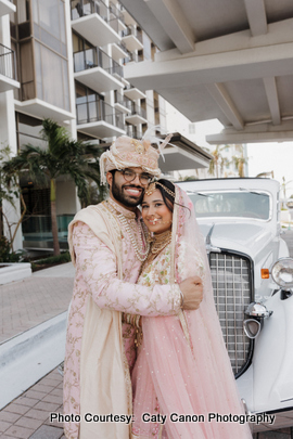 Ami and Vinny in traditional Indian wedding outfits embracing each other in front of a vintage white car.